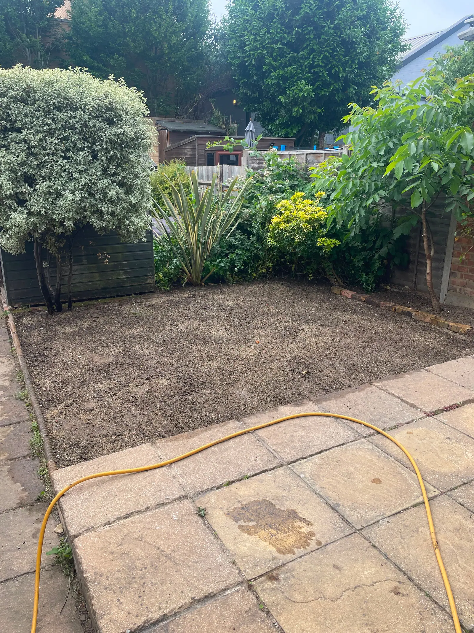 Back garden cleared to bare soil beside a patio, ready for new turf