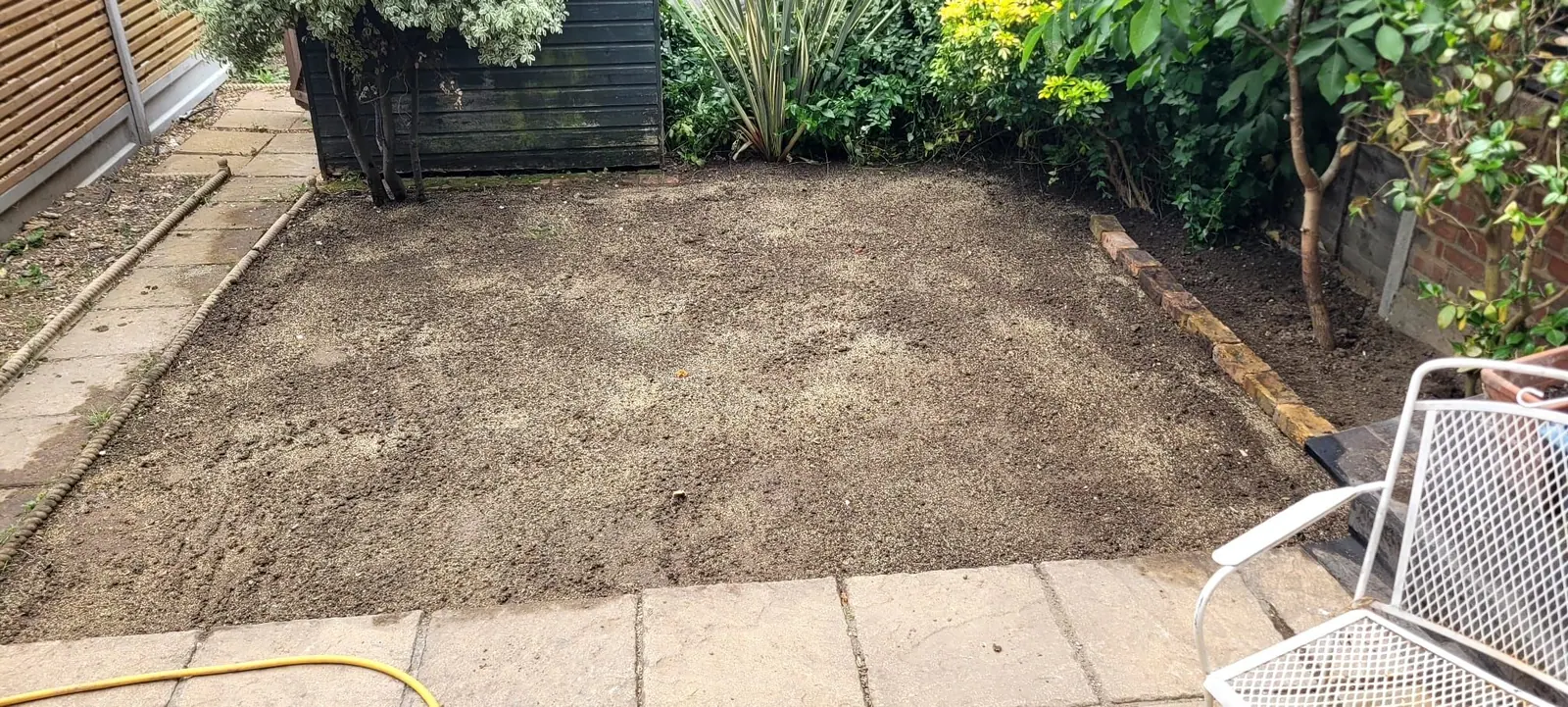 Garden rotavated and levelled ready for turf, with hose laid out and patio swept