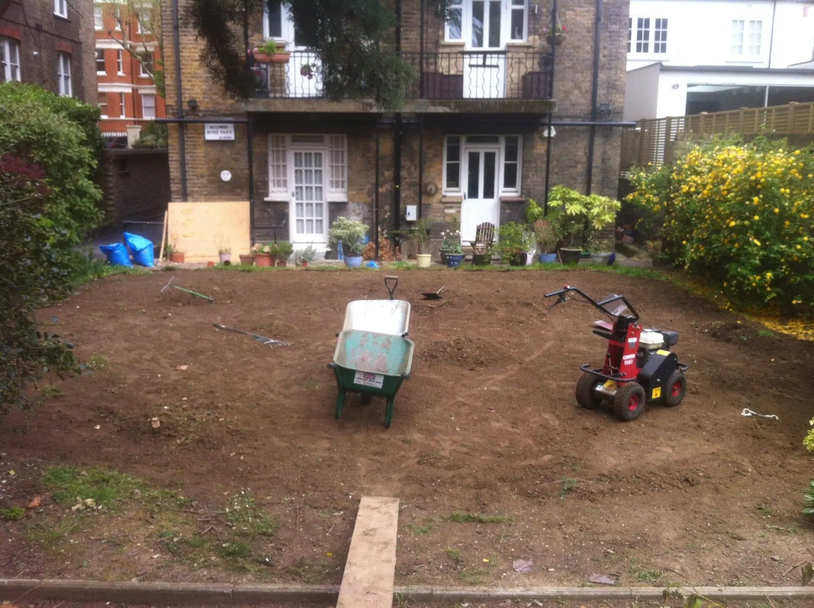 Back garden rotavated and levelled ready for new turf, with rotavator and barrow