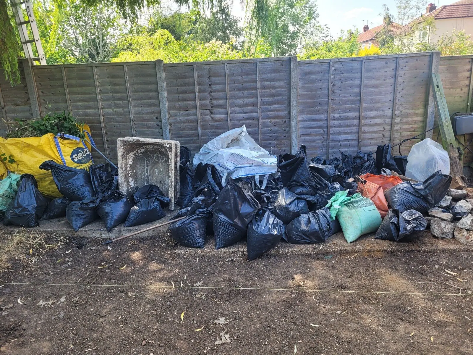 Garden waste bagged up along the fence ready for removal