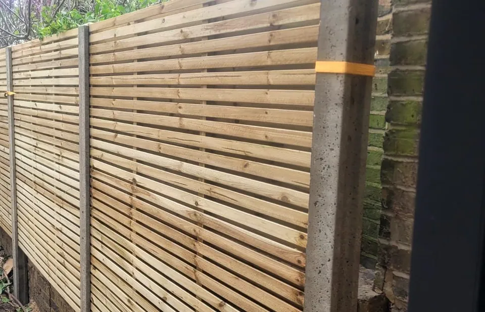 New horizontal slatted fence panels fitted between concrete posts along a garden boundary