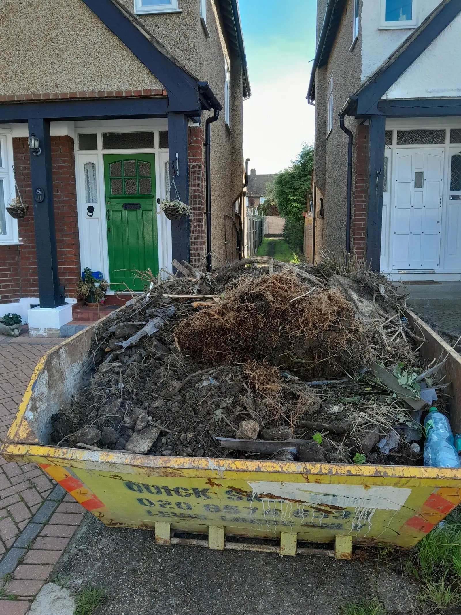Skip loaded with branches and garden waste outside a house
